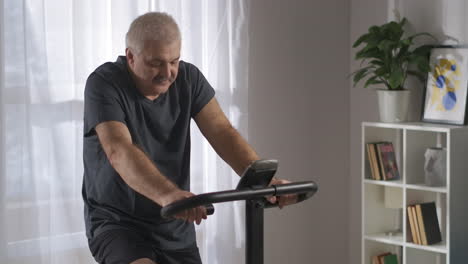caring-about-health-and-losing-weight-middle-aged-man-is-training-alone-at-home-on-stationary-bike-good-physical-condition